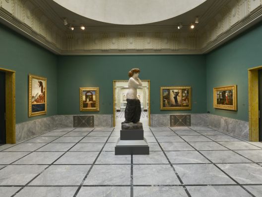 Quadratischer Ausstellungsraum mit grünen Wänden und halbnackter Skulptur